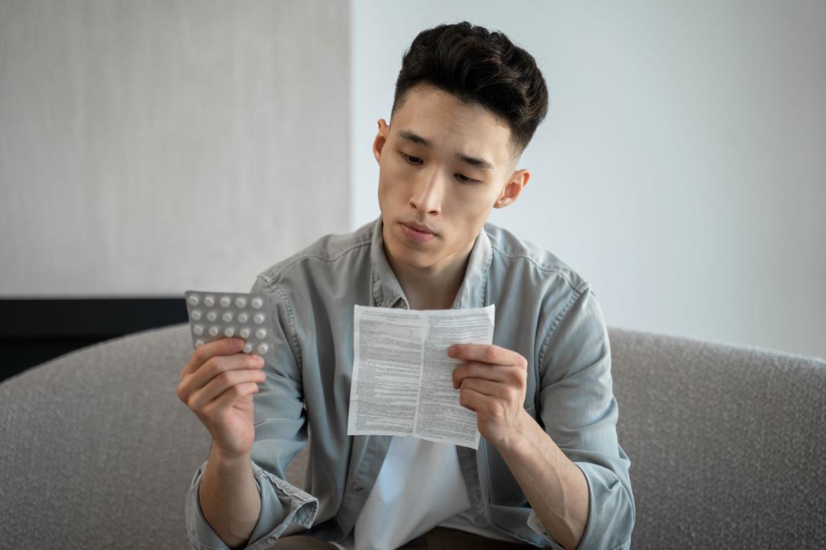 Jeune homme tenant une plaquette de médicaments pour soulager la douleur assis sur un canapé à la maison /Jongeman die een blisterverpakking met medicijnen vasthoudt voor pijnverlichting terwijl hij thuis op een bank zit Jeune homme tenant une plaquette de médicaments pour soulager la douleur assis sur un canapé à la maison /Jongeman die een blisterverpakking met medicijnen vasthoudt voor pijnverlichting terwijl hij thuis op een bank zit