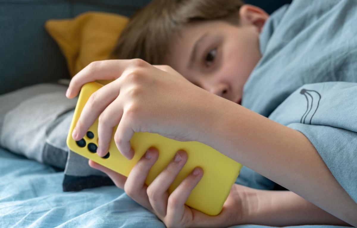 Jeune utilisant un smartphone dans son lit, une situation illustrant les enjeux liés à l’usage des réseaux sociaux chez les adolescents