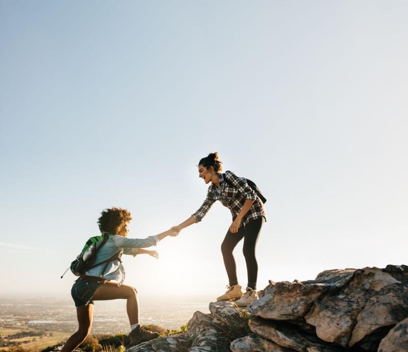 Young hiker helping a friend while hiking in the mountains