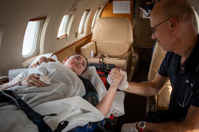 Enfant allongé dans un avion médicalisé, souriant et tenant la main d’un professionnel de santé, lors d’un rapatriement sanitaire.