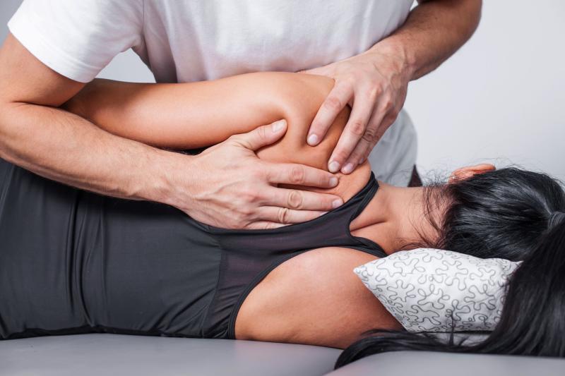 Séance de kinésithérapie : un thérapeute manipule l’épaule et le dos d’une patiente allongée sur le côté, pour soulager des tensions musculaires.