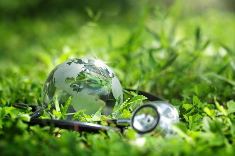 Globe terrestre en verre posé sur de l’herbe, accompagné d’un stéthoscope, symbolisant le lien entre santé humaine et environnement