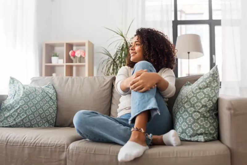 Jeune femme assise seule sur un canapé, regardant par la fenêtre, illustrant un moment de solitude