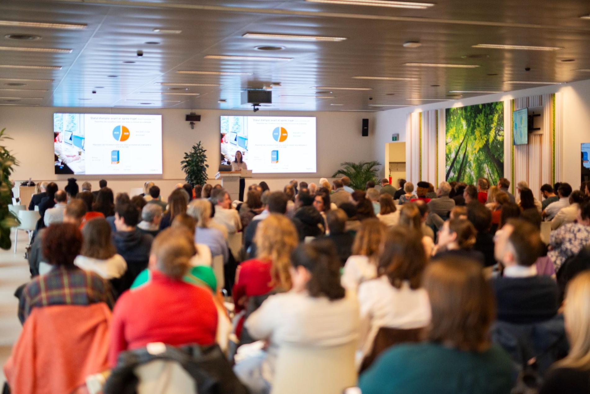 De spreker presenteert haar onderwerp en projecteert dia's voor een volle zaal