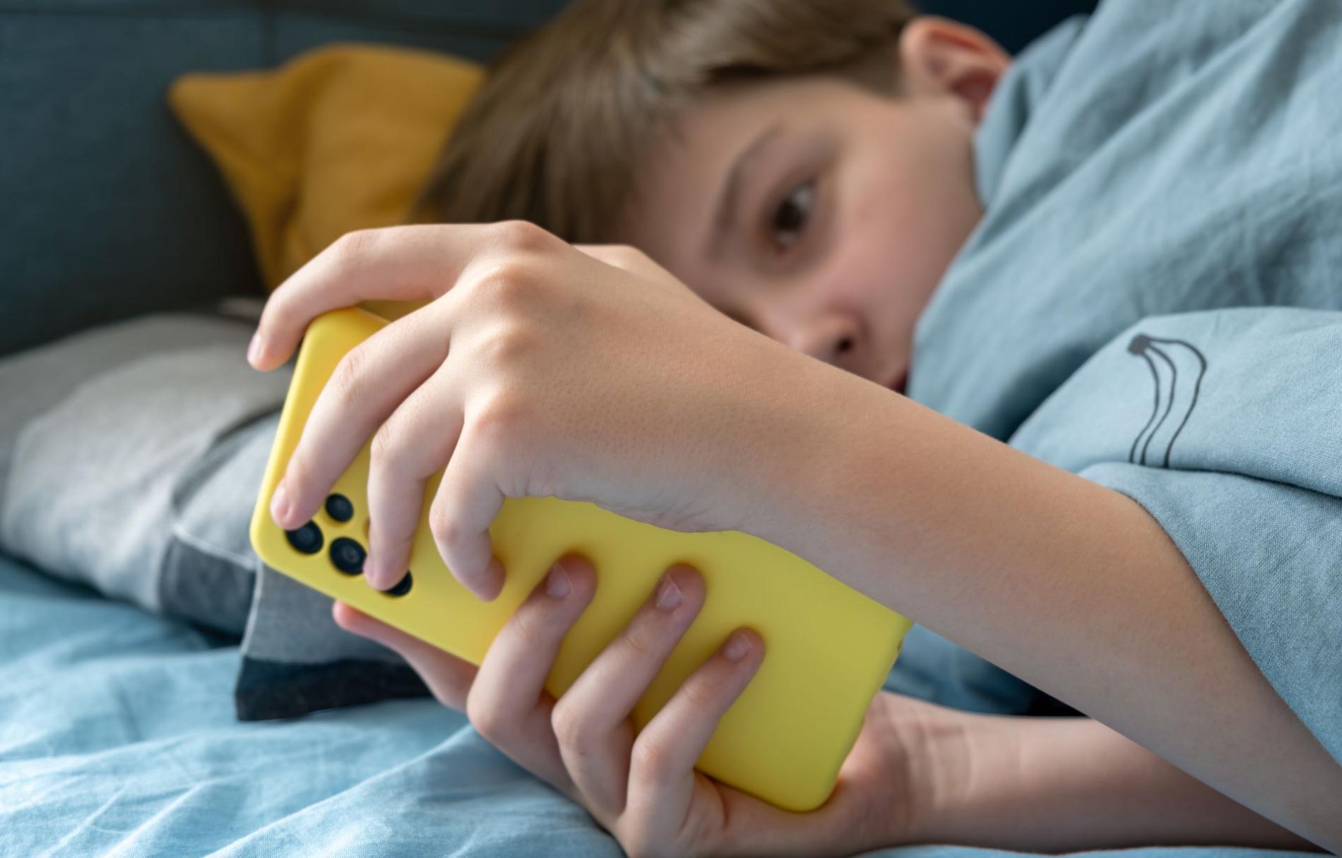 Jongere die een smartphone gebruikt in bed, als illustratie van de uitdagingen rond het gebruik van sociale media bij jongeren
