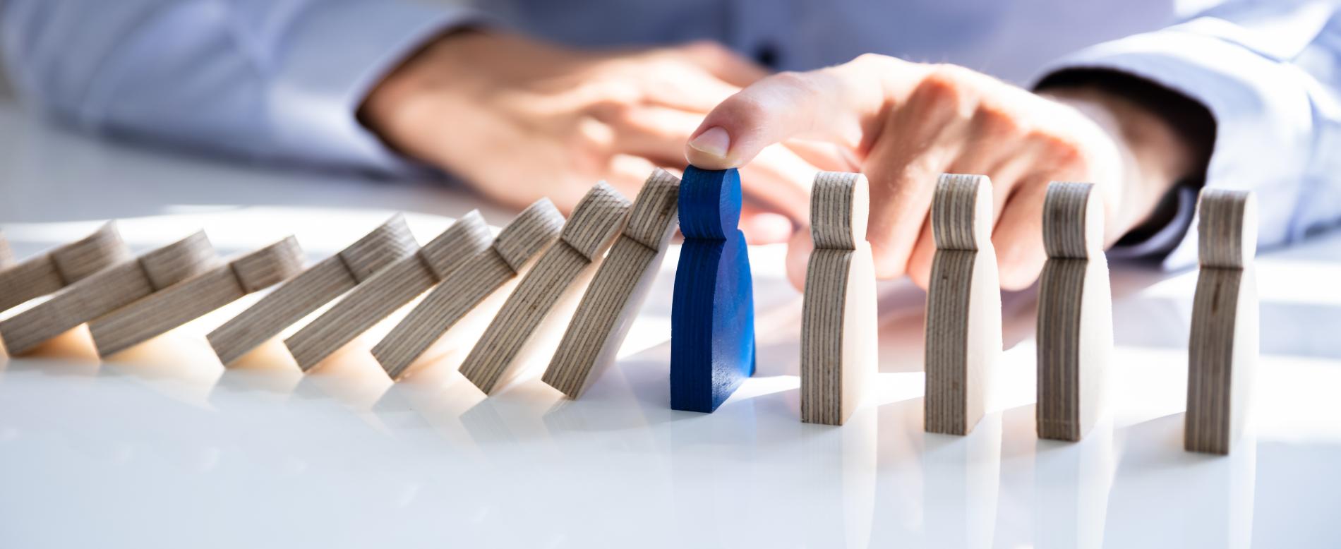 Une personne place un domino bleu debout parmi une rangée de dominos, illustrant le rôle de la prévention en santé.